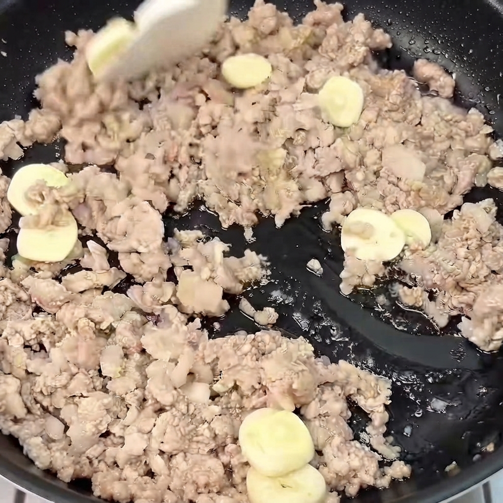 Geschnittener Ingwer und Knoblauch werden in einer Pfanne mit dem gebräunten Hackfleisch vermischt und angebraten.