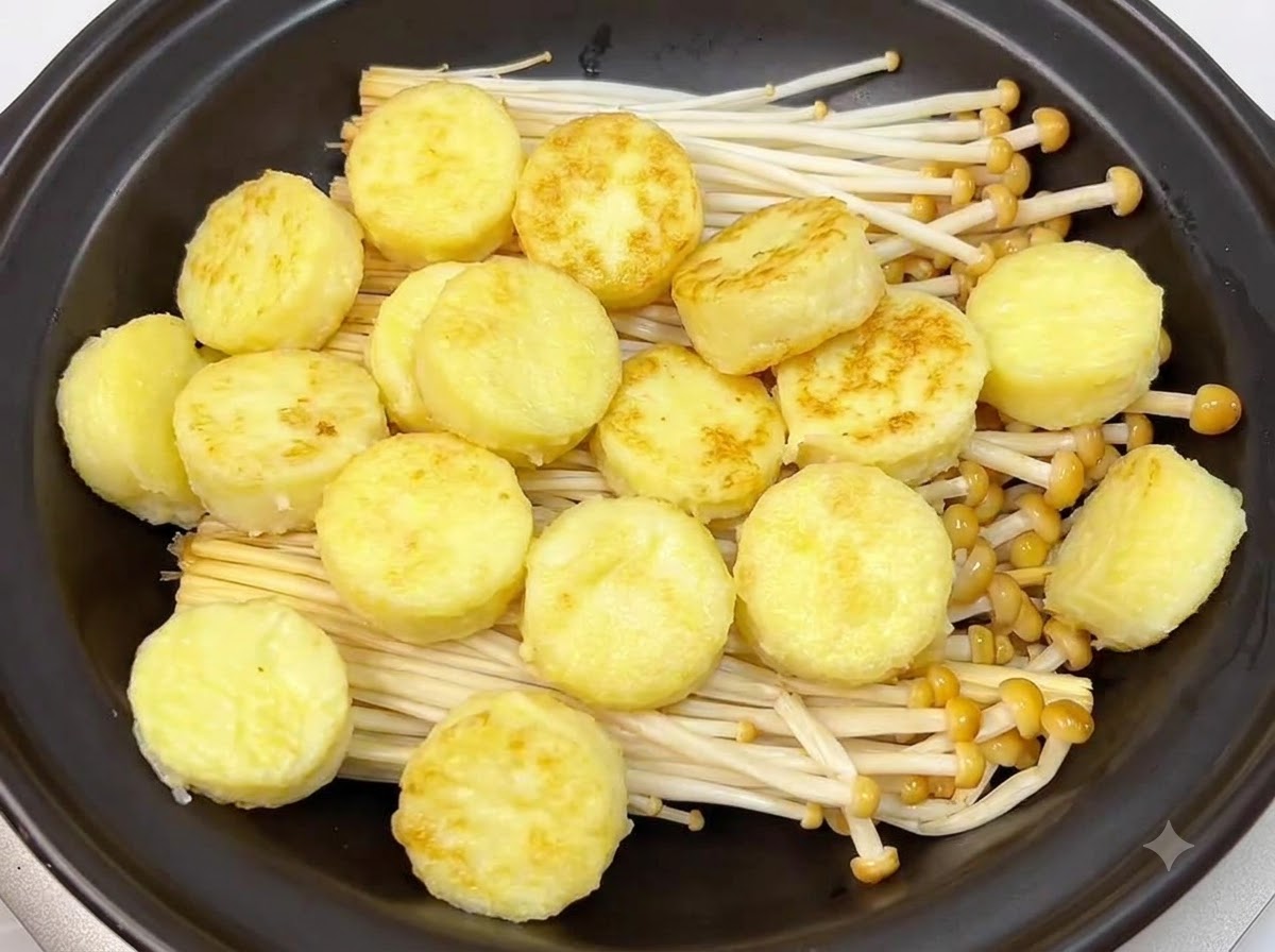 Goldbraun gebratene Scheiben japanischen Tofus sind ordentlich auf den Enoki-Pilzen im Inneren eines schwarzen Tontopfs angeordnet.