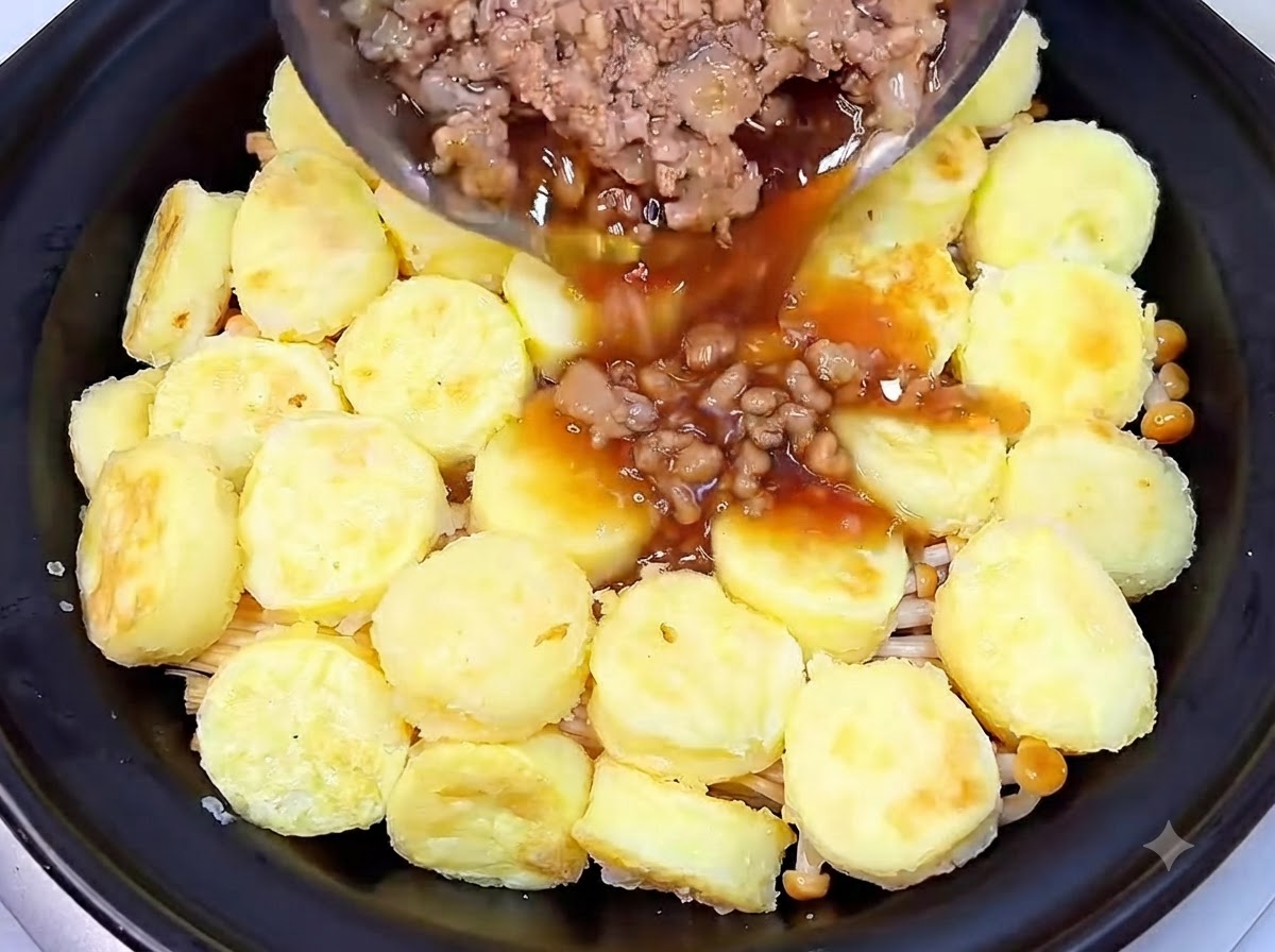 Gekochtes Hackfleisch und dunkle, herzhafte Sauce werden aus einer Pfanne über die Tofuschicht in den Tontopf gegossen.