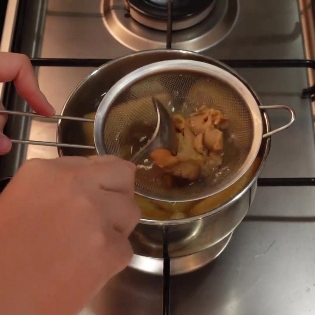 Helle Miso-Paste wird mit einem Löffel in einem Metallsieb in einem Topf mit heißer Suppe verrührt.