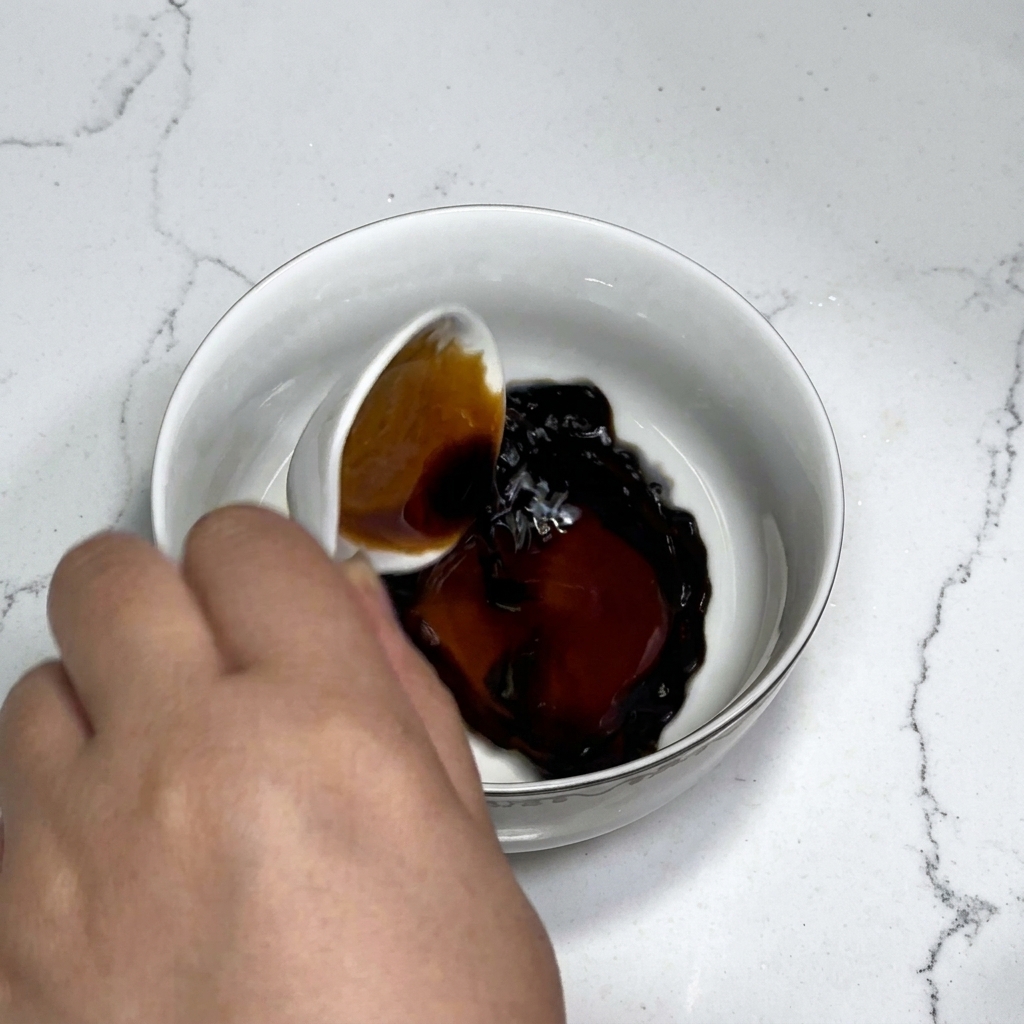 Saucenzutaten wie Sojasauce, Austernsauce, Zucker und Stärke werden in einer weißen Schüssel mit einem Löffel mit Wasser verrührt.