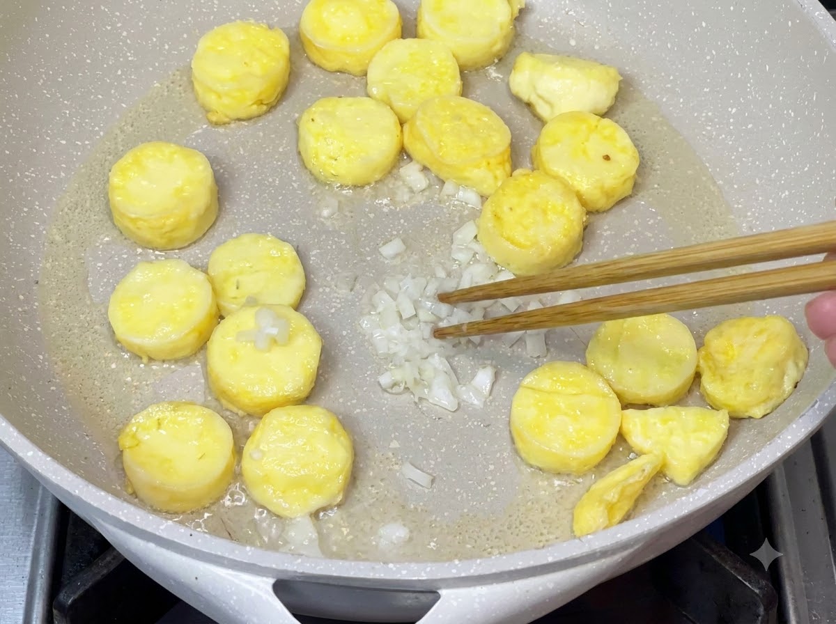 Gehackte Frühlingszwiebeln werden in der Pfanne angebraten, nachdem das überschüssige Öl entfernt wurde, um das Aroma zu entfalten.