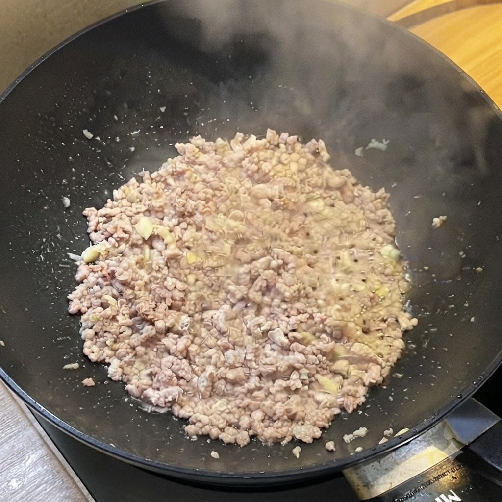 Ein Wok mit gebräuntem Hackfleisch, das dampft und mit flüssigen Saucen gewürzt wird.