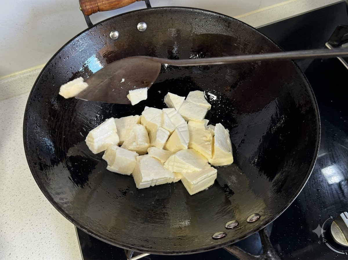 Ein Pfannenwender schneidet weiche Tofustücke in einem heißen Bratwok in Scheiben.