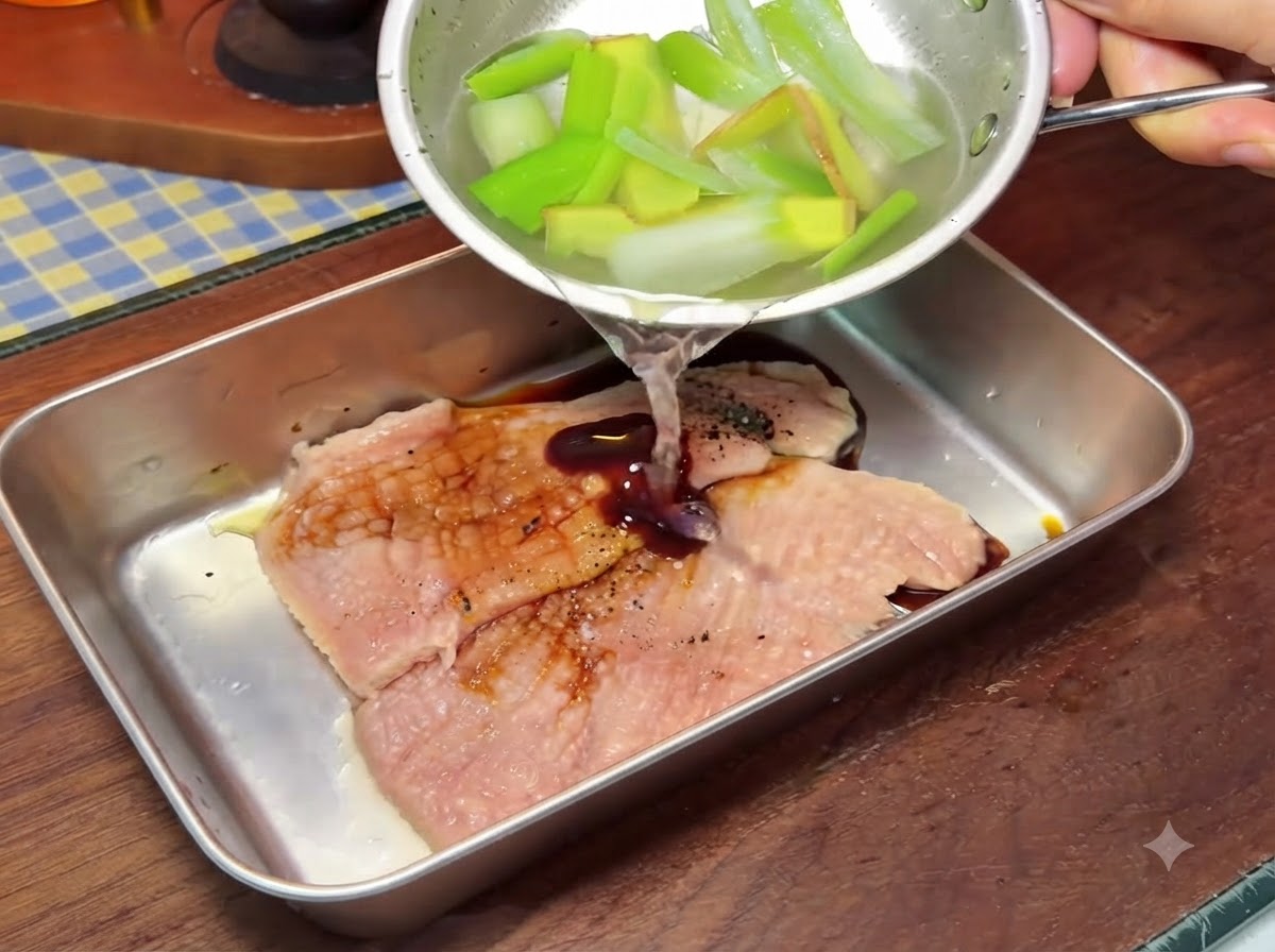 Eine kleine Schüssel gießt Flüssigkeit über Schweineschnitzel in einem größeren Metallbehälter während der Zubereitung.