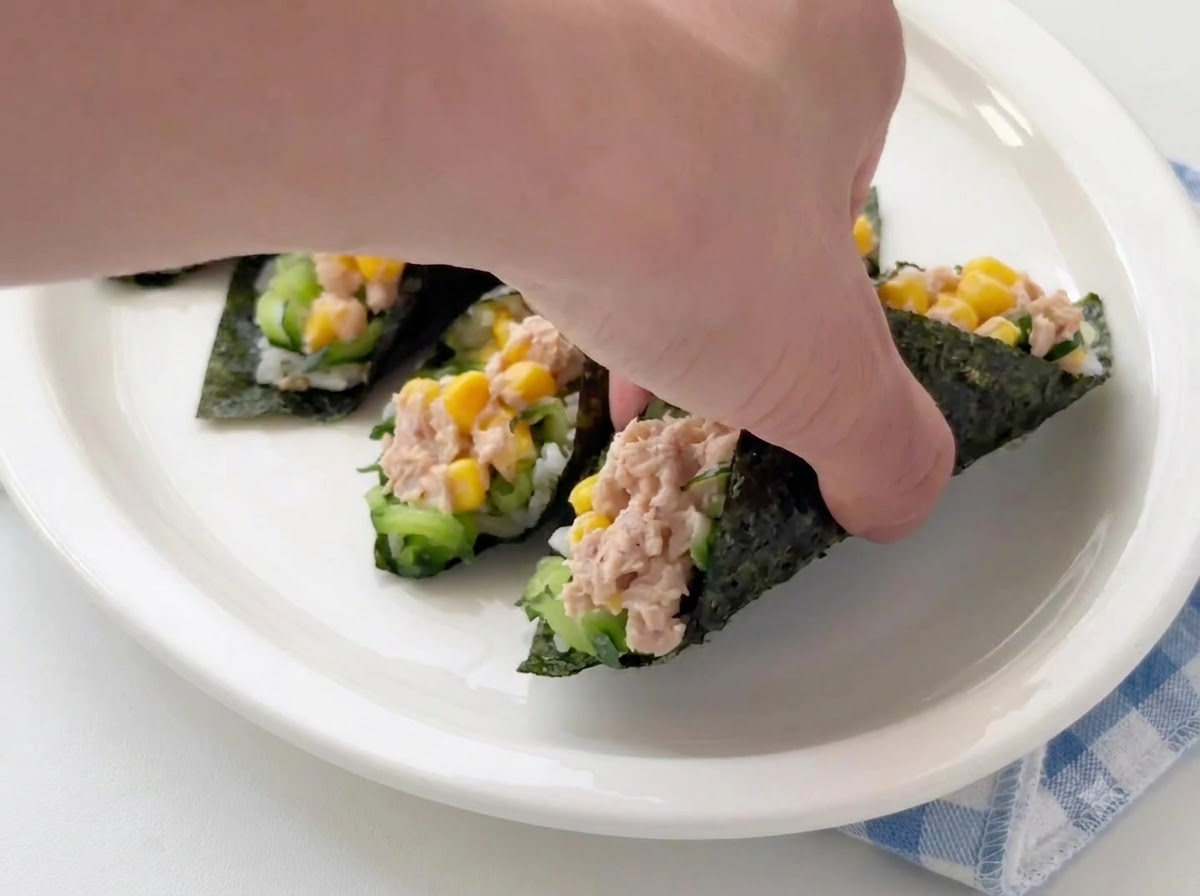 Eine Hand platziert oder richtet fertige Thunfisch-Algen-Reis-Rollen auf einem weißen Servierteller an.