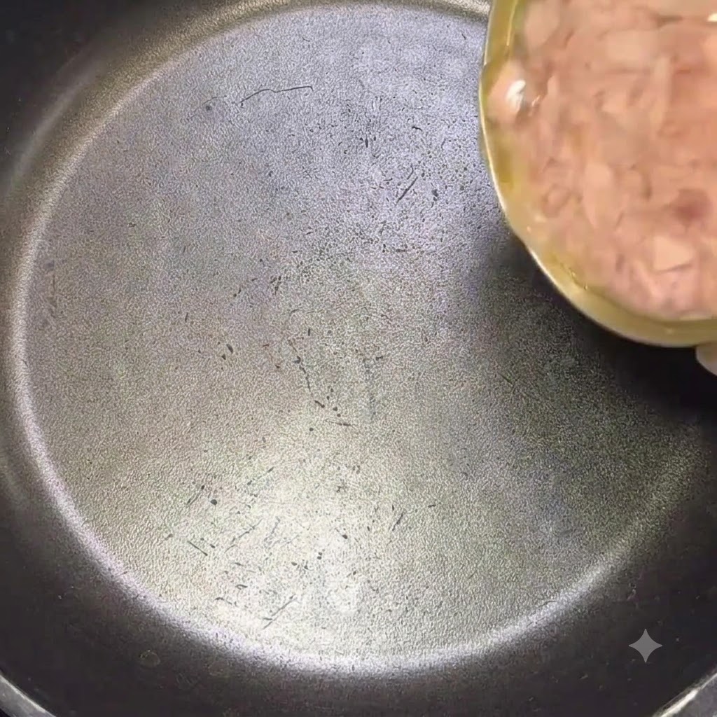 Eine große Dose Thunfisch wird samt Öl in eine schwarze Pfanne gegossen.