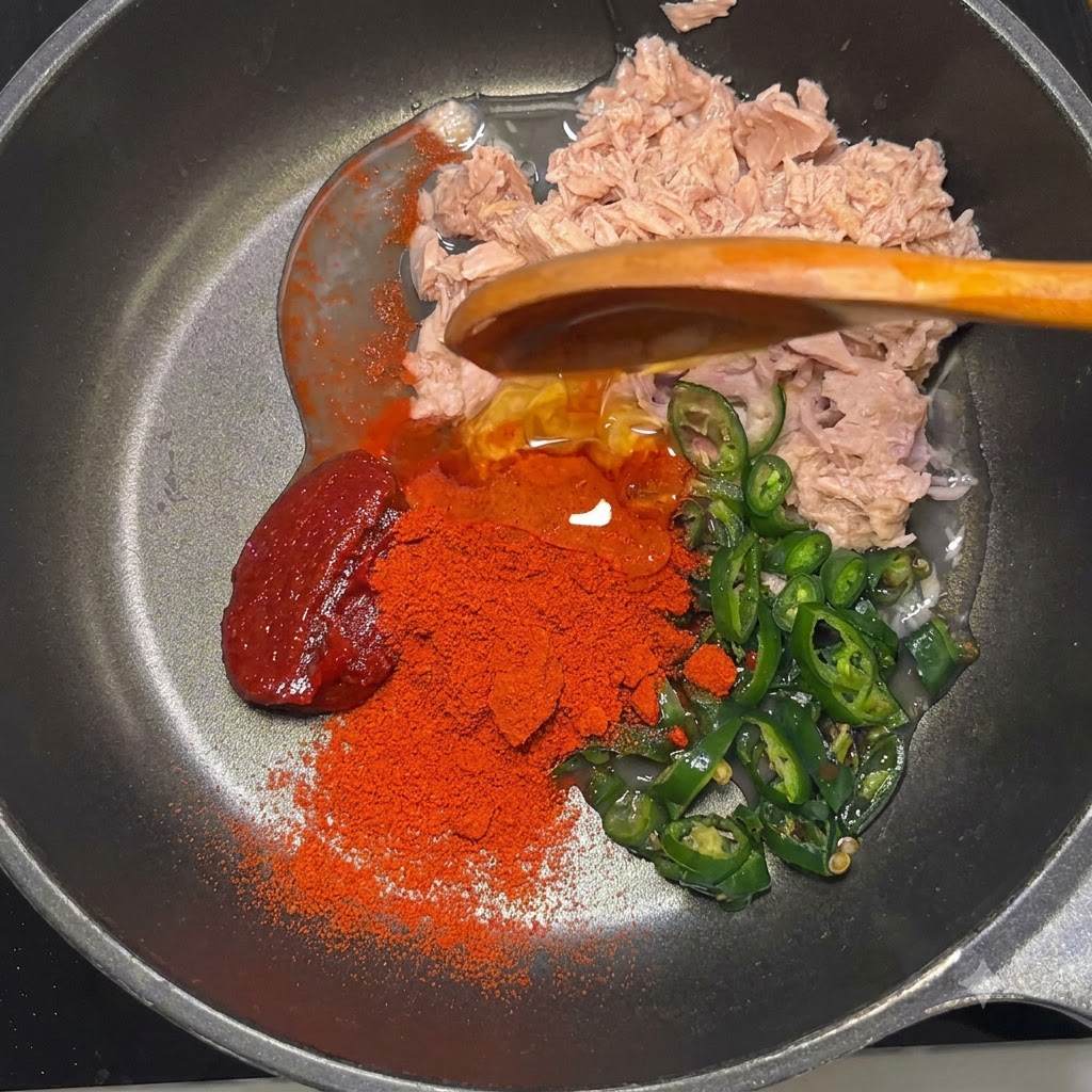 Gochujang-Paste, rotes Gochugaru-Pulver, Maissirup und Mayonnaise liegen in der Pfanne über dem Thunfisch und den Chilis.