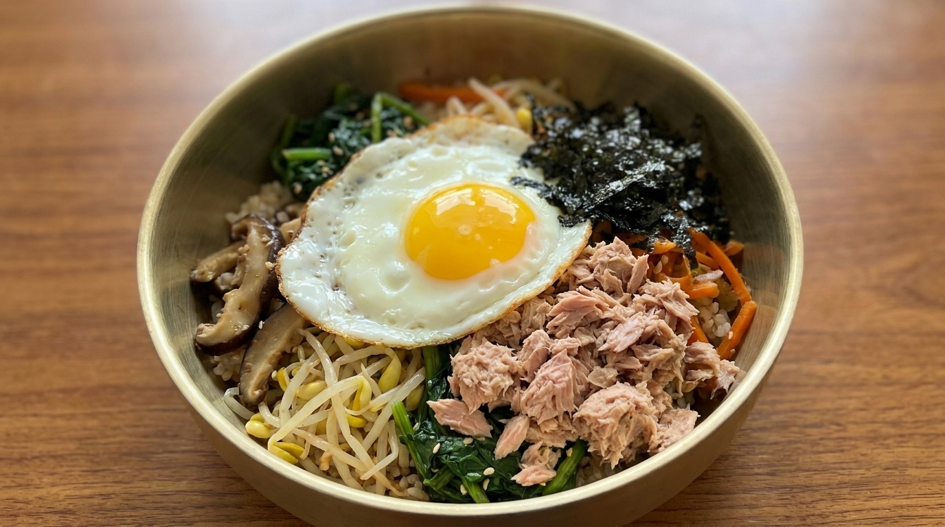 Eine farbenfrohe Schüssel Thunfisch-Bibimbap mit gewürztem Reis, frischem Gemüse, Pilzen, Algenflocken, Dosenthunfisch und einem Spiegelei.