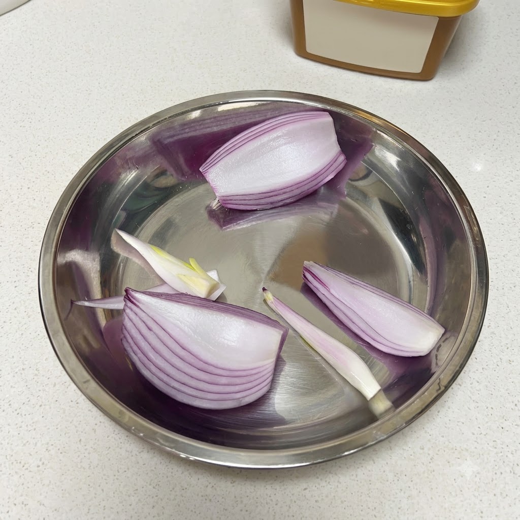 Geschnittene rote Zwiebel, ein halber Apfel und geschälte rohe Knoblauchzehen in einer Metallschüssel.