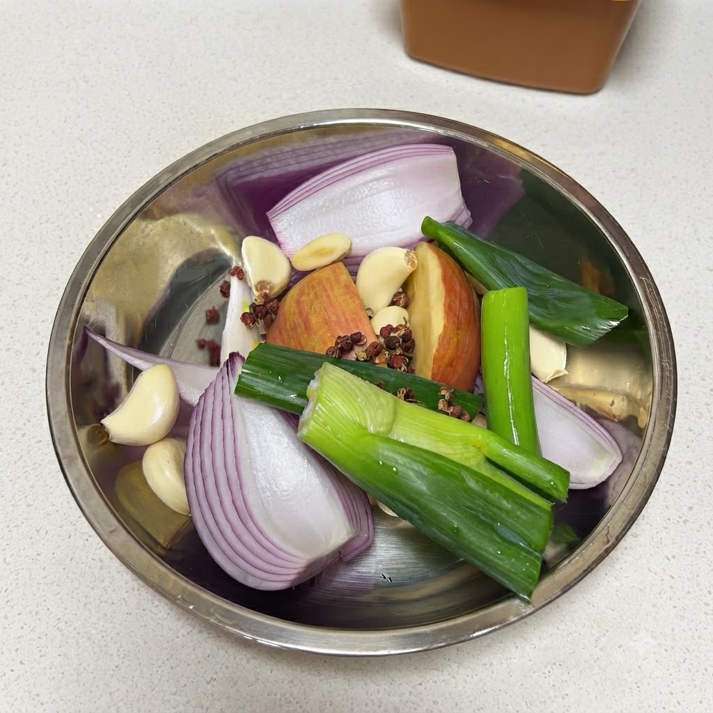 Frische Frühlingszwiebeln werden in eine Metallschüssel mit Zwiebel, Apfel, Knoblauch, Pfefferkörnern und Lorbeerblatt geschnitten.