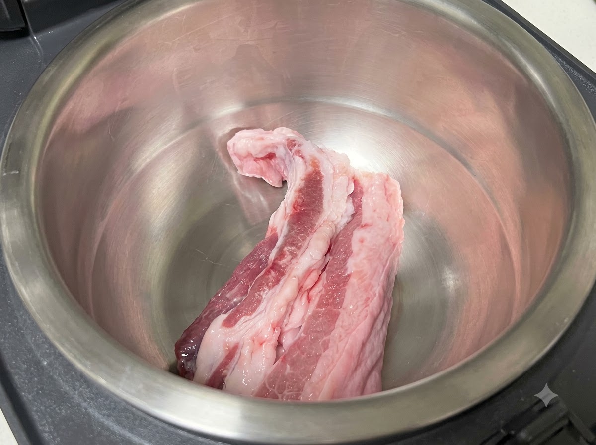 Rohe Schweinebauchstreifen im leeren Edelstahltopf eines Reiskochers.