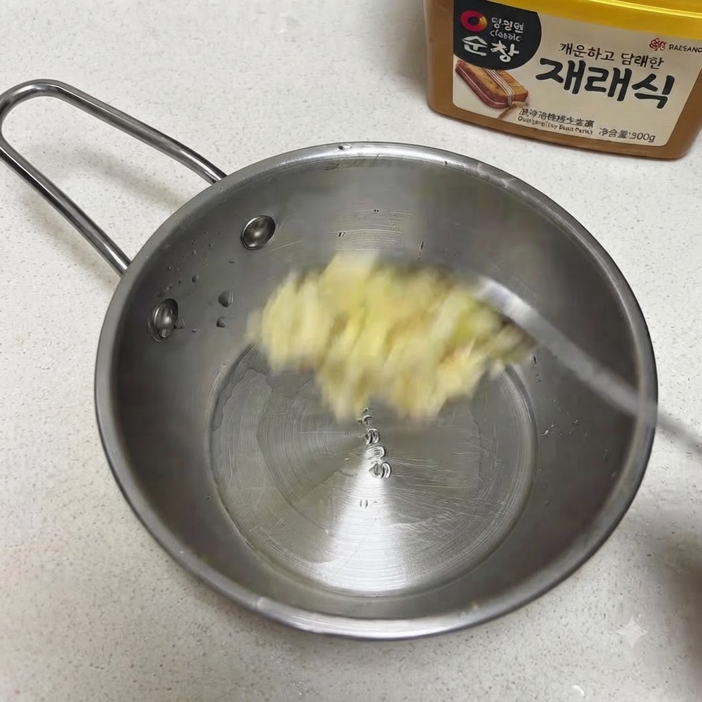 Gehackter Knoblauch und Sesamsamen werden in eine kleine Edelstahlpfanne gegeben.