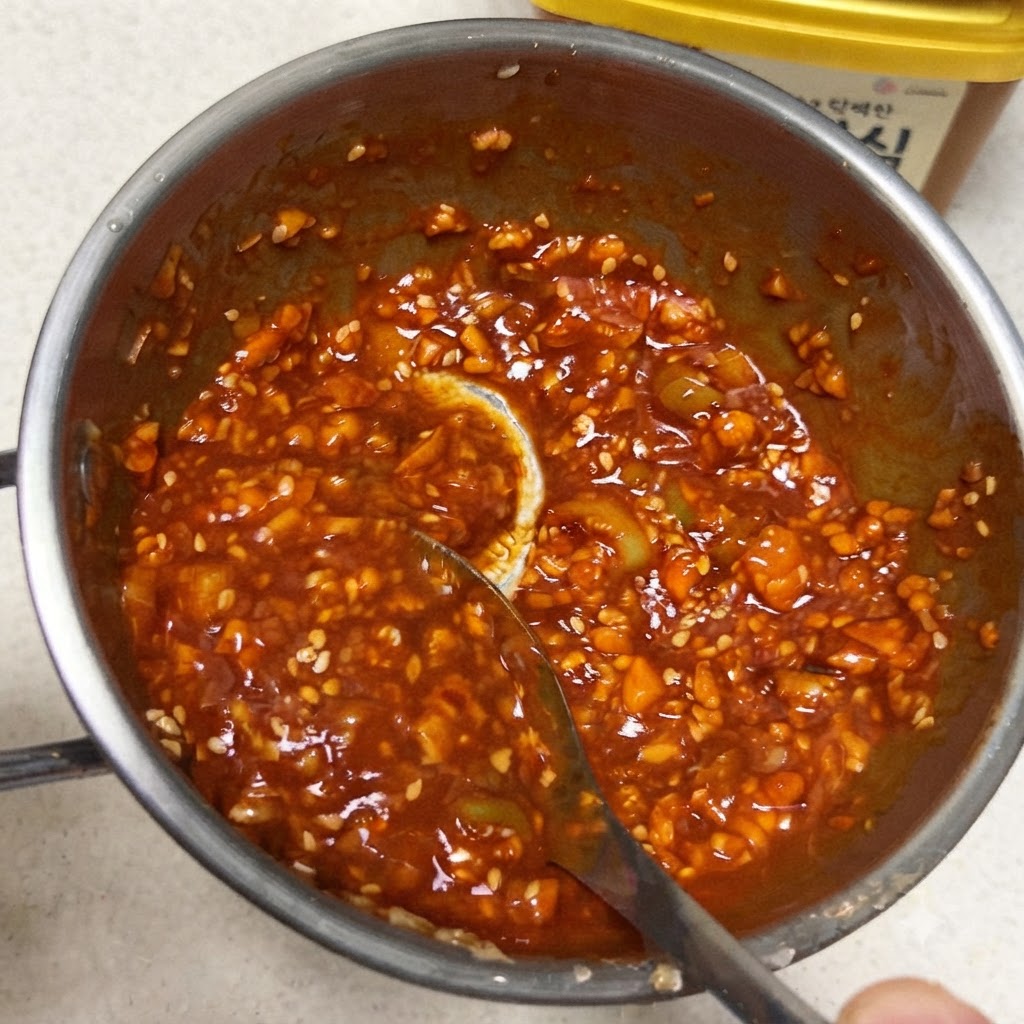 Ein Löffel rührt eine dicke, leuchtend rote koreanische Dip-Sauce in einer kleinen Metallpfanne um.