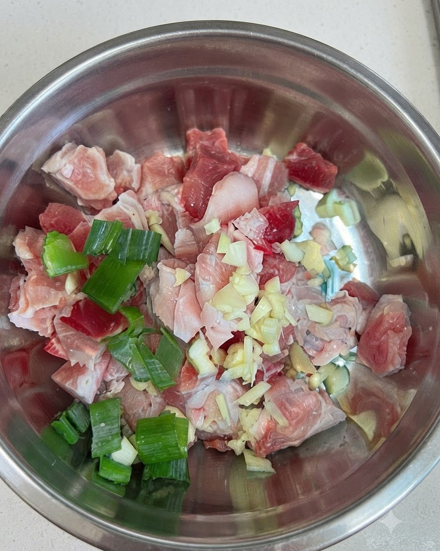 Rohe Schweinebauchwürfel in einer Schüssel mit Knoblauch, Frühlingszwiebeln und roter Chilipaste.