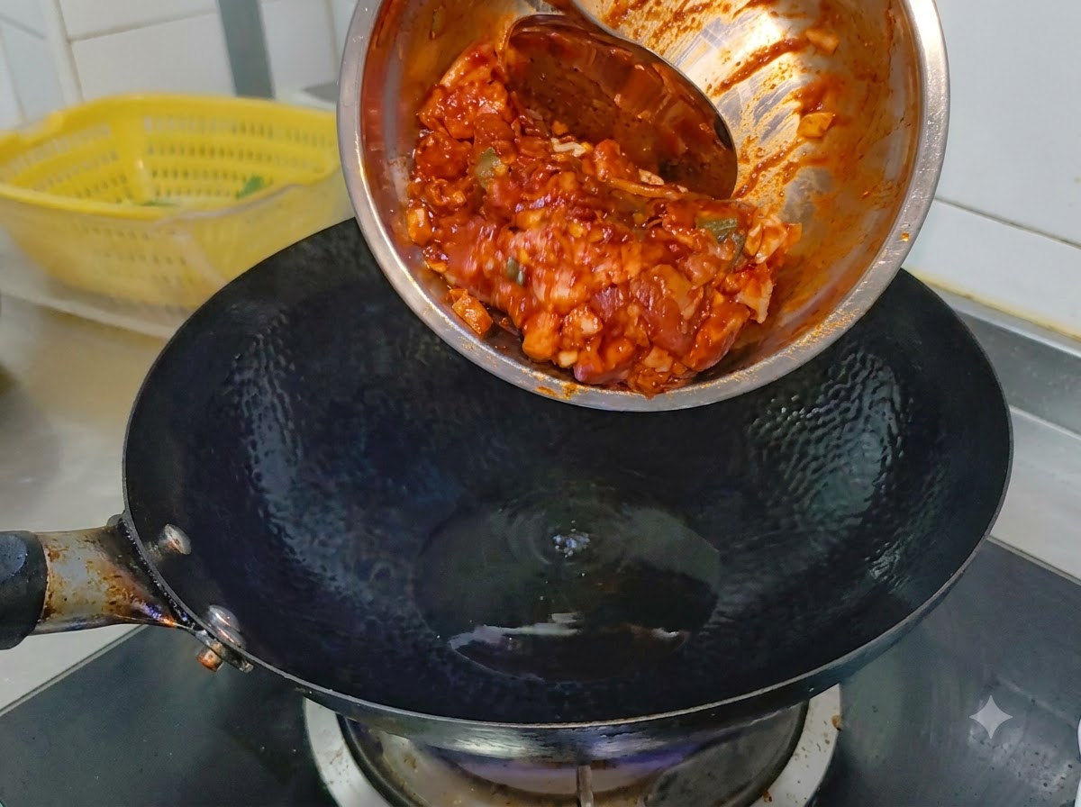Mariniertes, scharfes Schweinefleisch gleitet aus einer Metallschüssel in einen heißen, rauchenden schwarzen Wok mit Speiseöl.