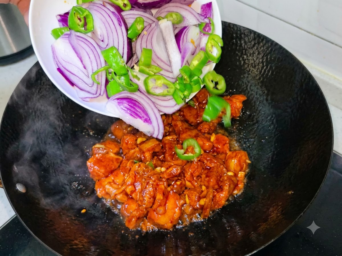 Rote Zwiebelscheiben und grüne Chilischoten werden von einem Teller zum bratenden Schweinefleisch in den Wok gegeben.