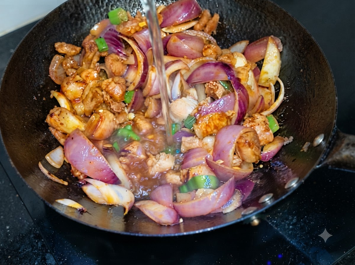 Wasser wird von oben in einen Wok mit gebratenem Schweinebauch und roten Zwiebeln gegossen.