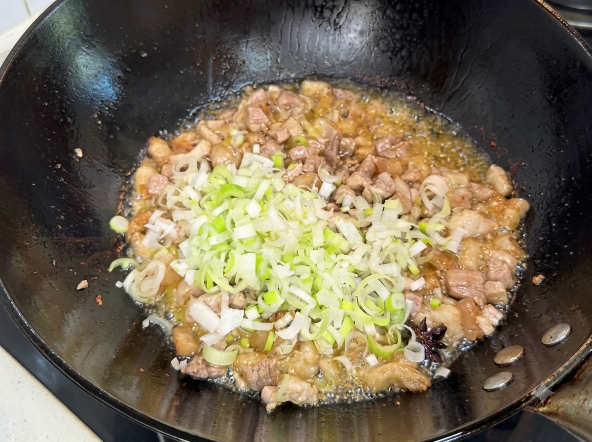 Gehackte grüne Frühlingszwiebeln werden in die gebratene Fleischmischung im Wok gerührt.