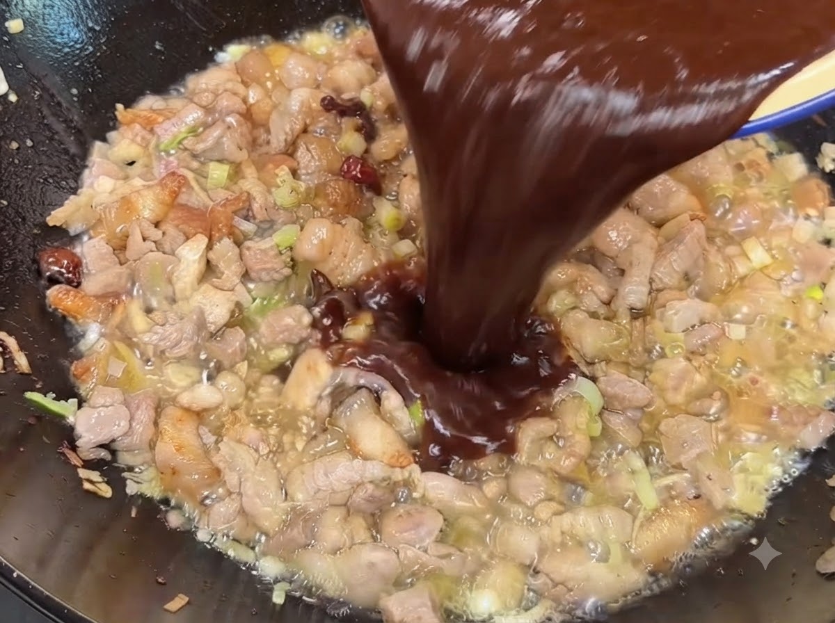 Dunkle Soja- und Bohnenpastensauce wird in den Wok über das gekochte Fleisch gegossen.