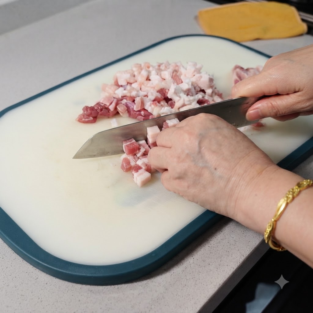 Nahaufnahme von rohem Schweinebauch, der auf einem weißen Schneidebrett mit einem Beil in kleine Würfel geschnitten wird.
