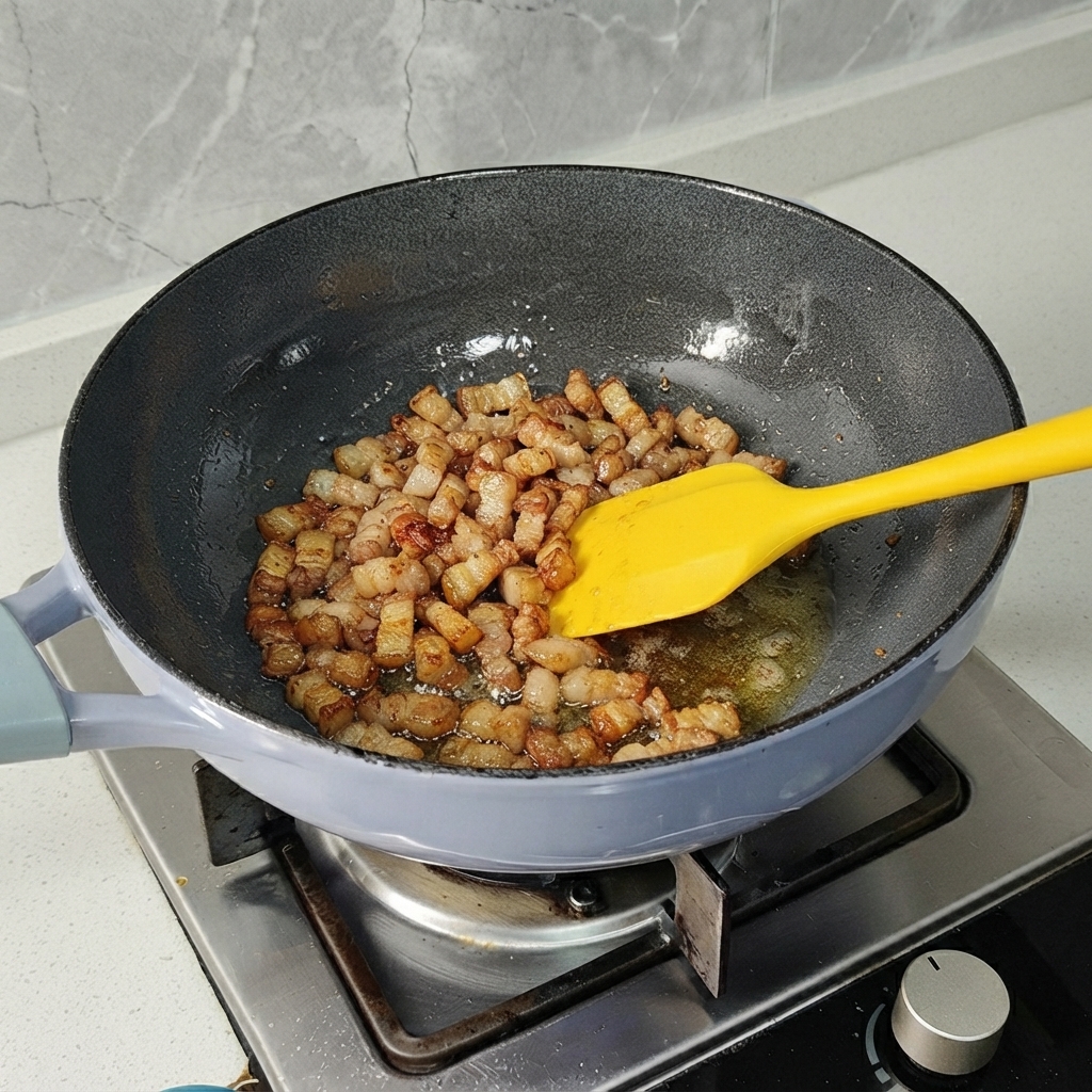 Schweinebauchstücke werden in einer Pfanne mit einem gelben Spatel angebraten, bis sie leicht gebräunt sind.