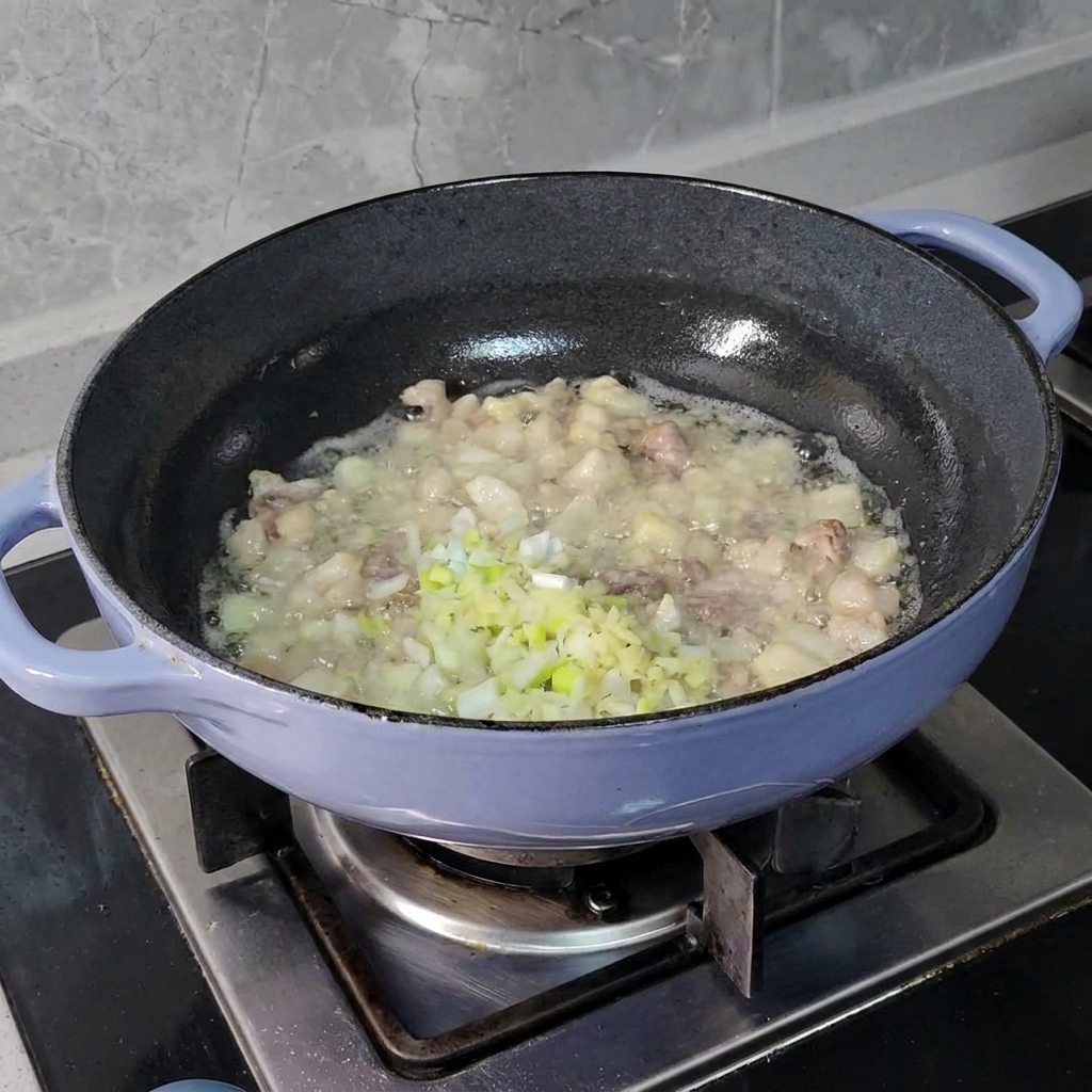 Fein gehackte Frühlingszwiebeln, Ingwer und Knoblauch werden in einer dunklen Pfanne zu brutzelnden Fleischstücken gegeben.