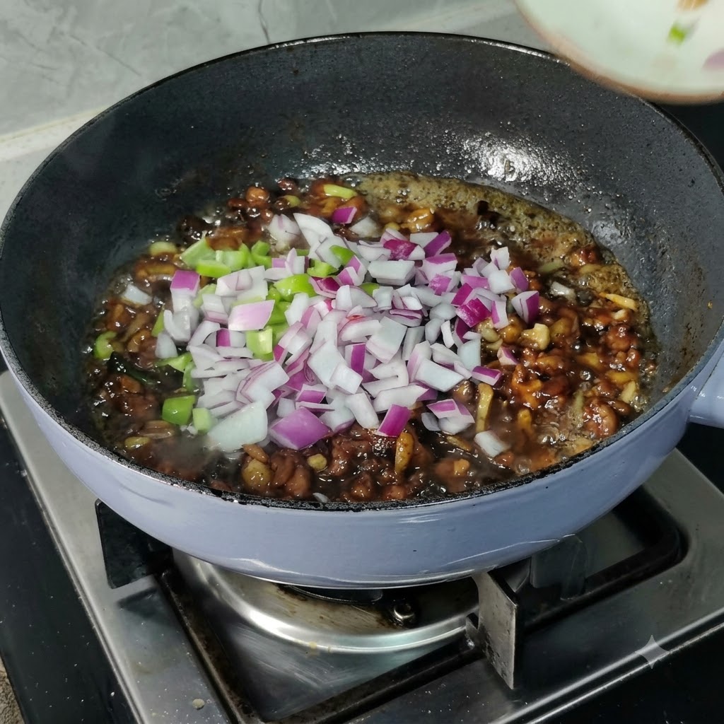 Gewürfelte rote Zwiebeln und grüne Paprika sind über einer köchelnden dunklen Sauce in einer Pfanne verstreut.