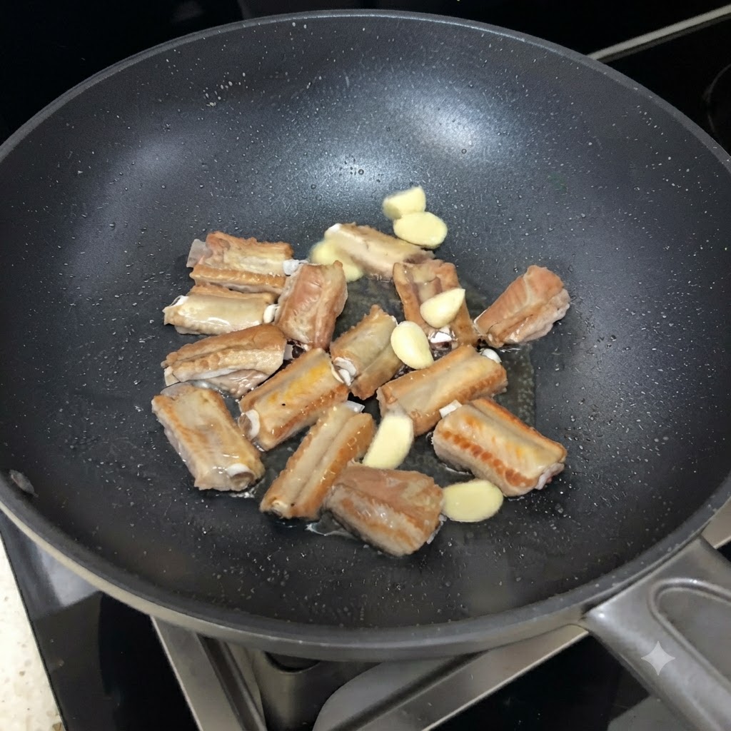 Knoblauchscheiben verteilt zwischen den anbratenden Schweinerippchen in der Pfanne.