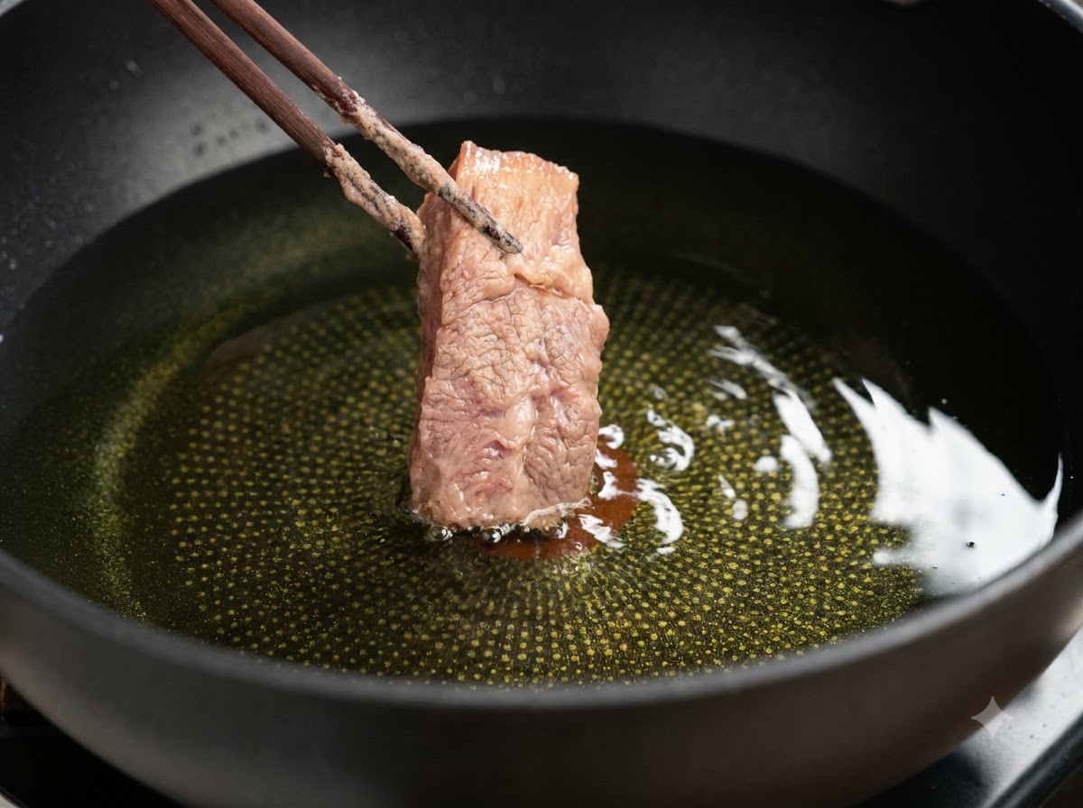 Ein Stück paniertes Schweinerippchen wird mit Stäbchen in heißes Öl abgesenkt.