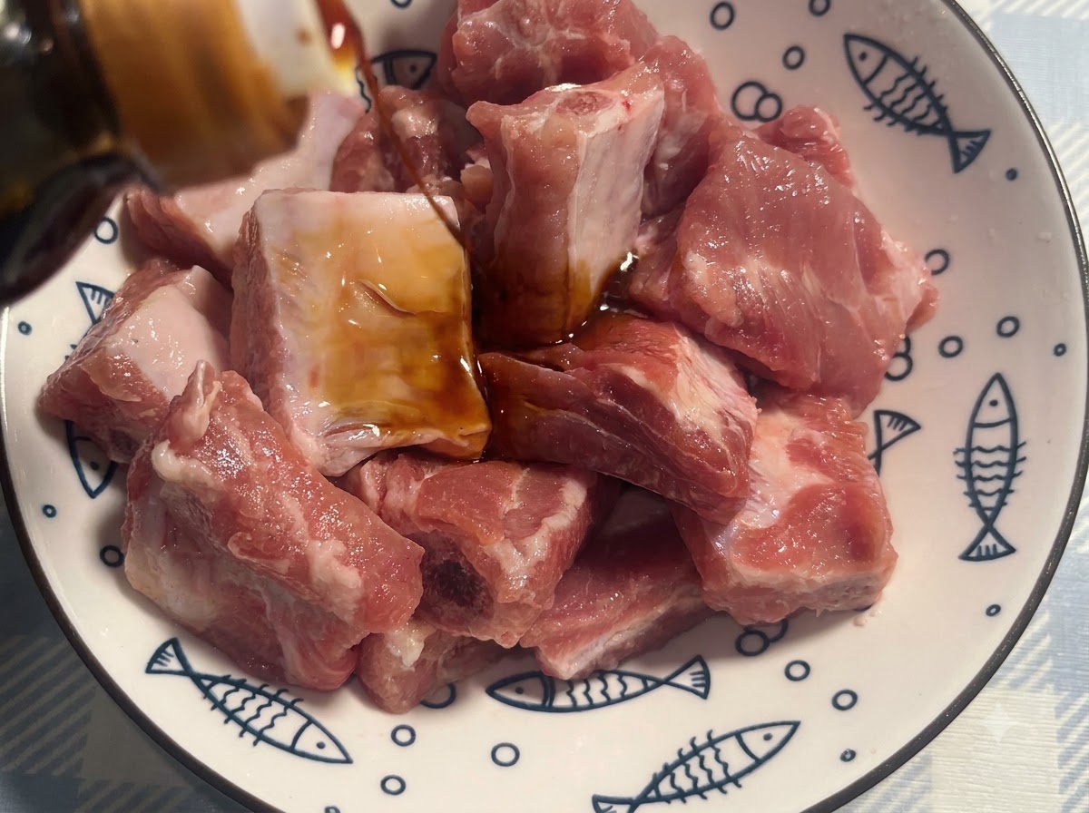 Schweinerippchen in einer weißen gemusterten Schüssel werden mit dunkler Sojasauce gewürzt.