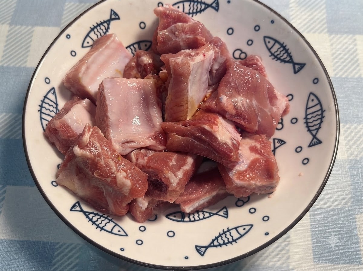 Mit Handschuhen versehene Hände wenden und mischen die gewürzten Schweinerippchen auf einem weißen Teller.