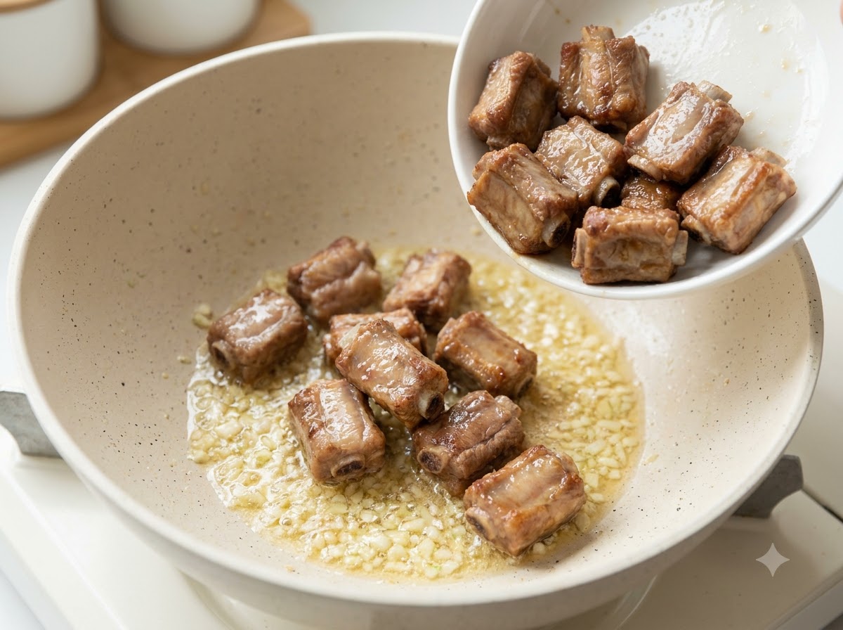 Vorher angebratene Schweinerippchen werden in eine Pfanne mit sautiertem Knoblauch und Butter gegeben.