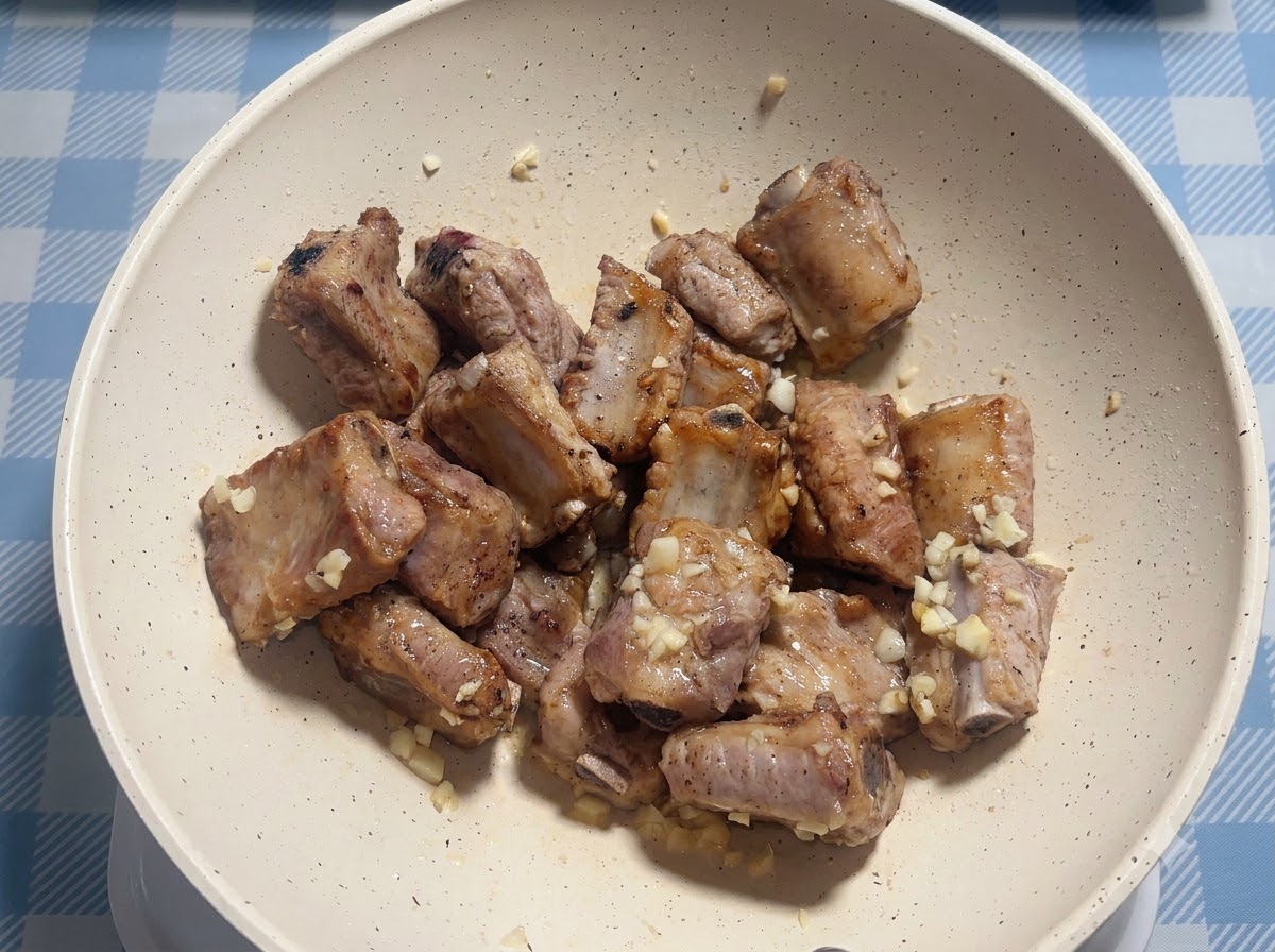 Schweinerippchen werden in einer weißen Bratpfanne mit Sauce gewürzt.