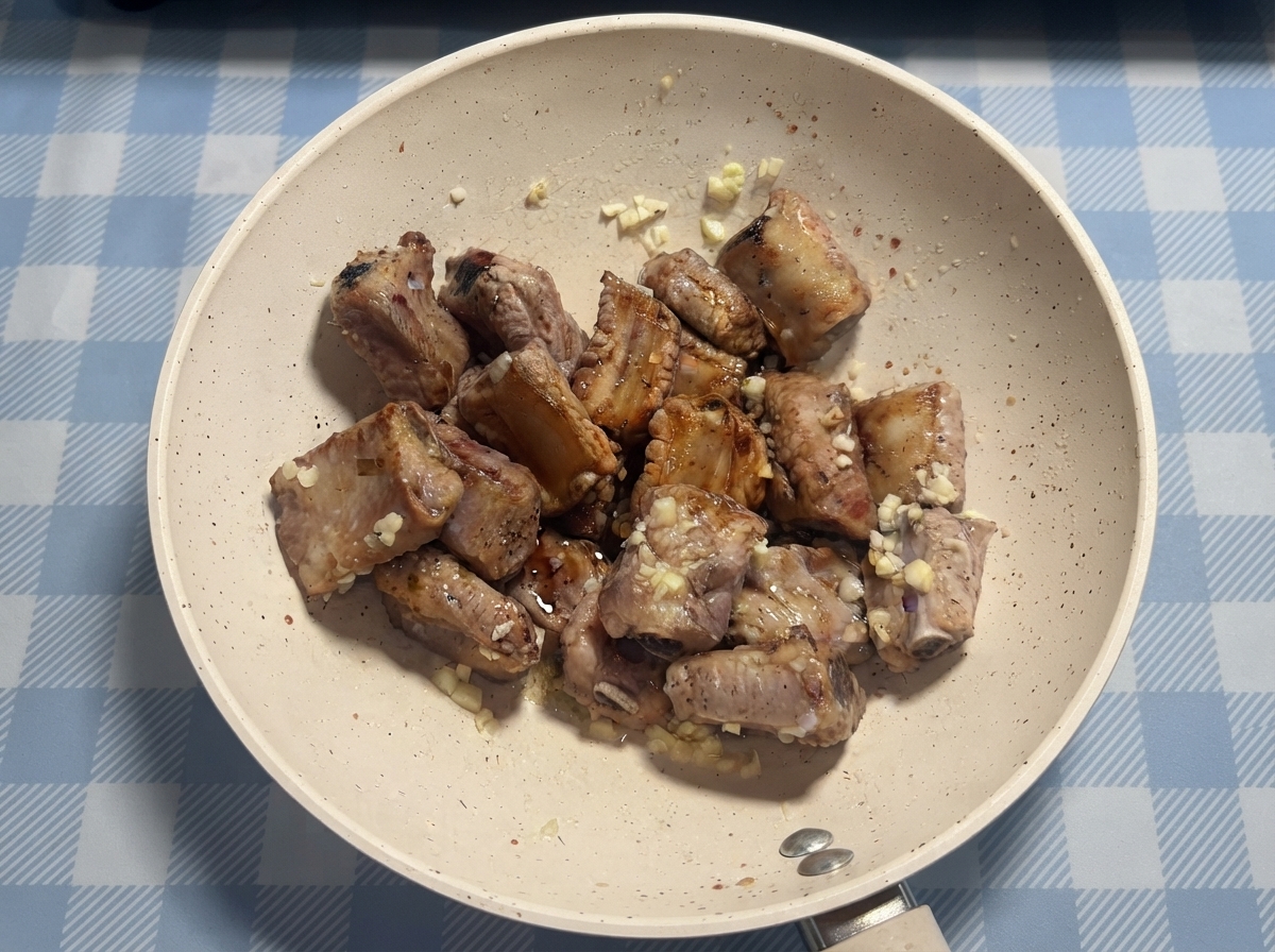 Schweinerippchen werden vor dem finalen Schwenken in einer Pfanne mit Sauce und Honig beträufelt.