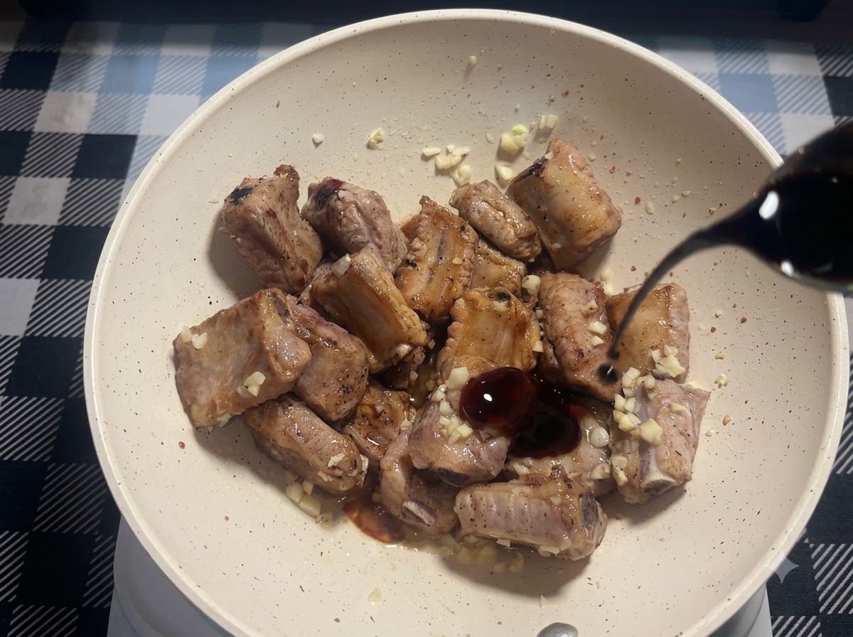Ein kleiner Strahl dunkler Sojasauce wird in die Pfanne mit gebratenen Schweinerippchen und gehacktem Knoblauch gegossen.