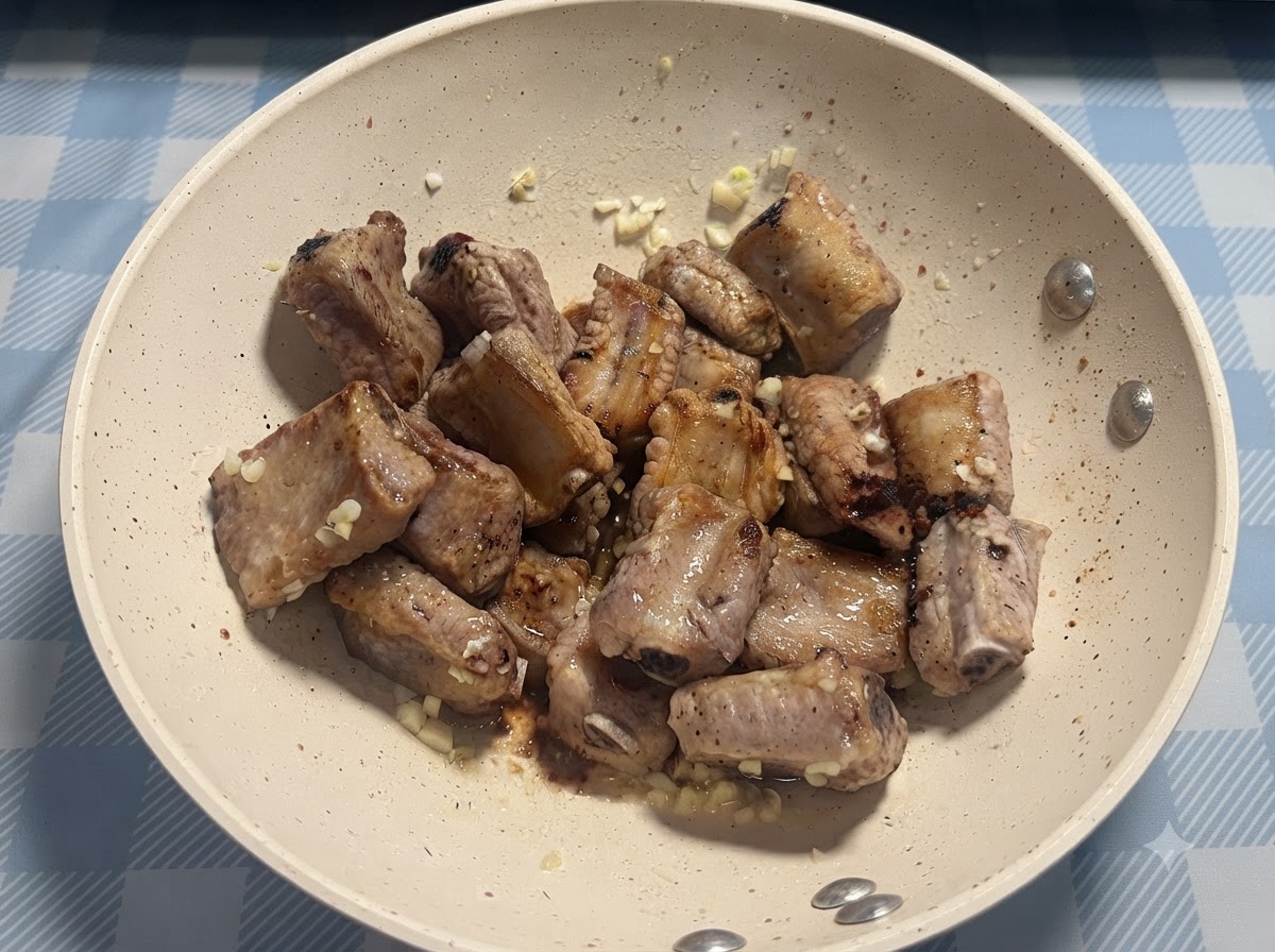 Eine Prise Salz wird direkt über die in der Pfanne gebratenen Schweinerippchen gestreut.