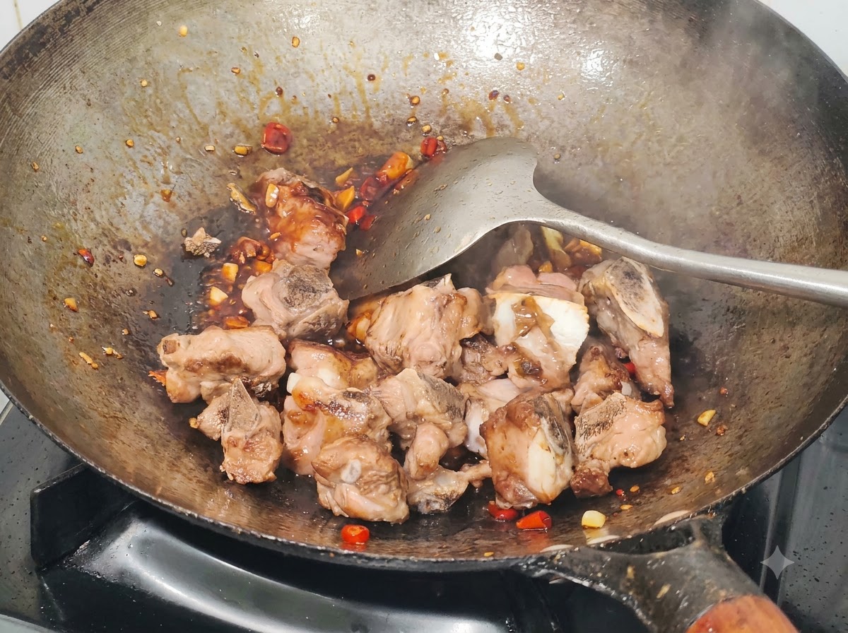 Gebratene Schweinerippchen werden mit einem Metalldampfschieber in einem Wok mit Sauce, gehackten Chilis und Knoblauch vermengt.
