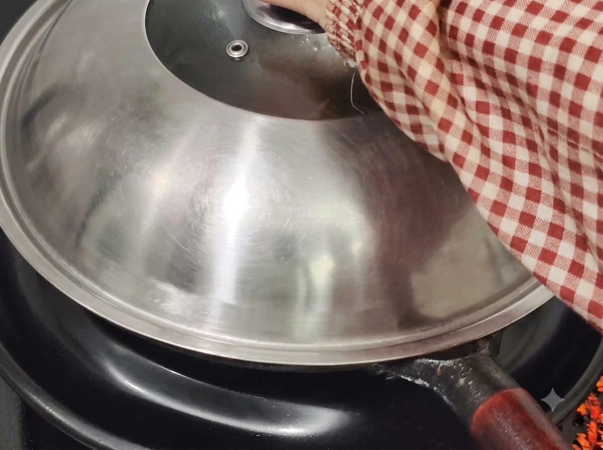 Ein Metalldeckel bedeckt den Wok auf einem Herd, gehalten von einer Hand in einem rot-weiß karierten Ärmel.