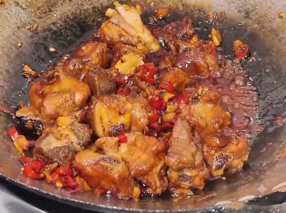 Schweinerippchen köcheln in einer dicken, dunklen Sauce mit sichtbaren Stücken von rotem Chili und Knoblauch in einem Wok.