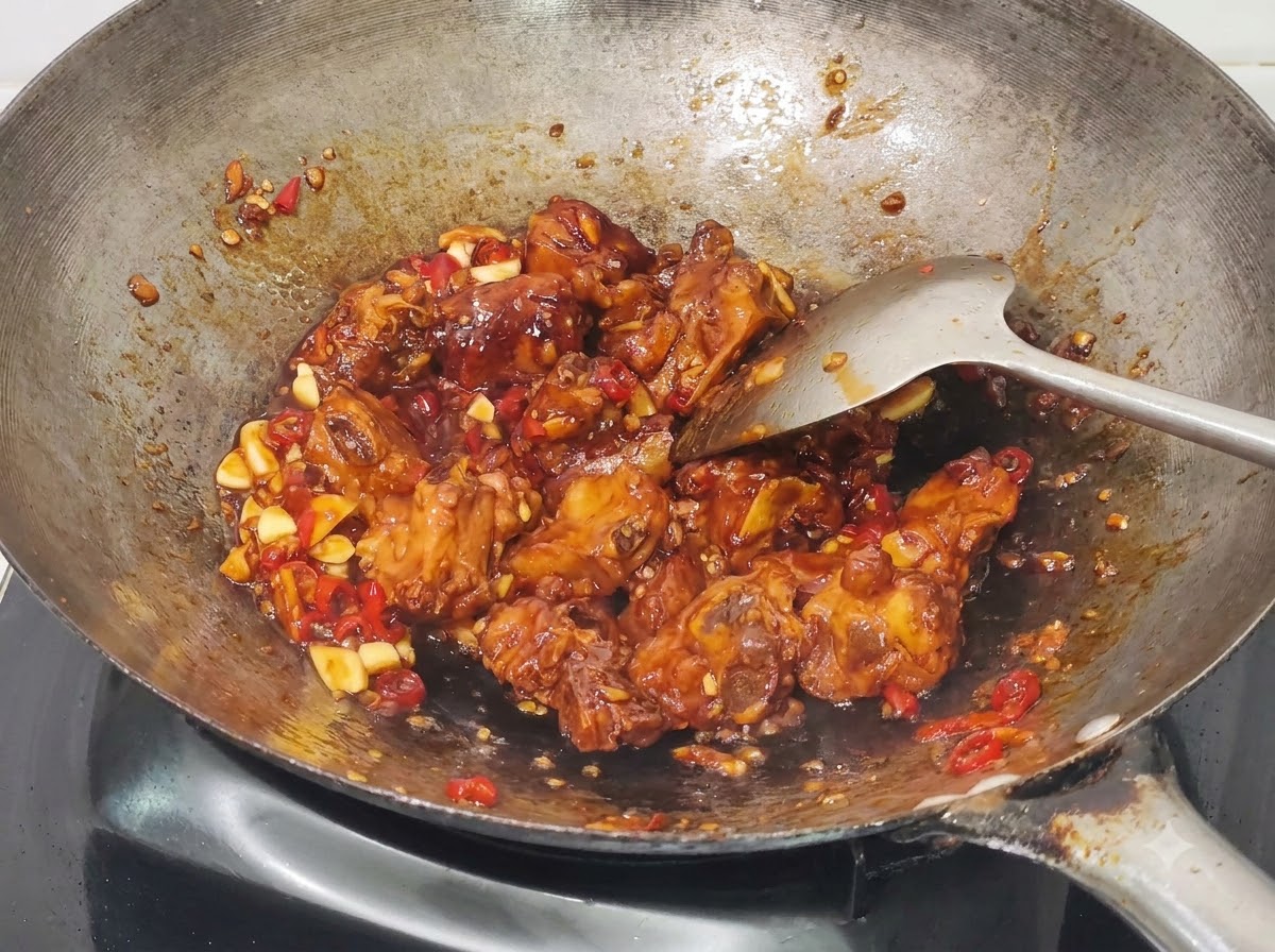 Gehackte Frühlingszwiebeln werden in die gekochten Honig-Knoblauch-Schweinerippchen im Wok eingearbeitet.