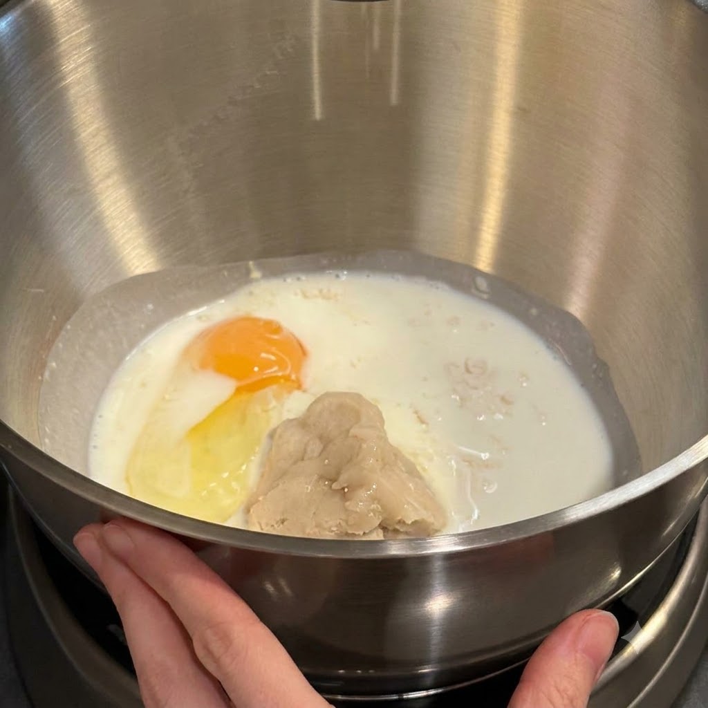 Rührschüssel mit Mehl, Milch, einem Eigelb und Tangzhong-Paste bereit zum Mischen.