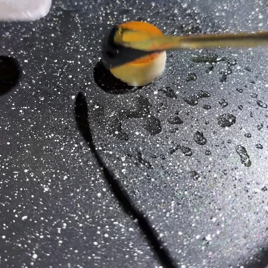 Gelbe Eierflüssigkeit wird in die Mitte eines kleinen, hohlen Pilzrings in einer heißen, gesprenkelten Pfanne gespritzt.