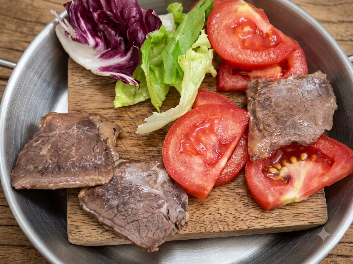 Frischer Salat, aufgeschnittene Tomaten und gekochte Fleischstücke auf einem kleinen Holzbrett angeordnet.