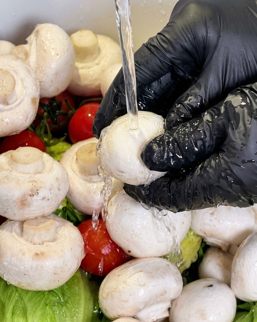 Ein weißer Champignon wird unter fließendem Wasser abgespült.