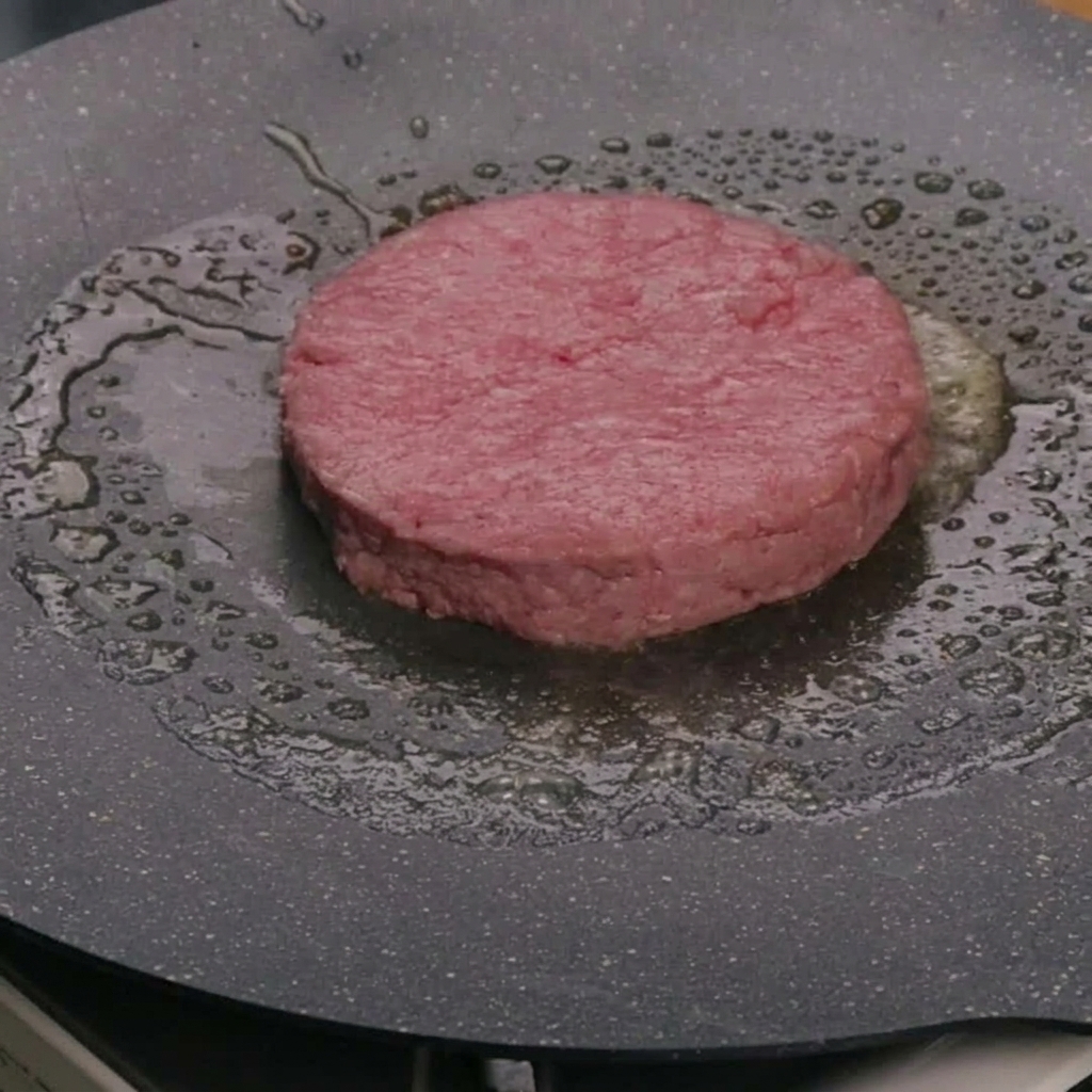 Ein rohes Rinderpatty gart in Butter in einer heißen Bratpfanne.