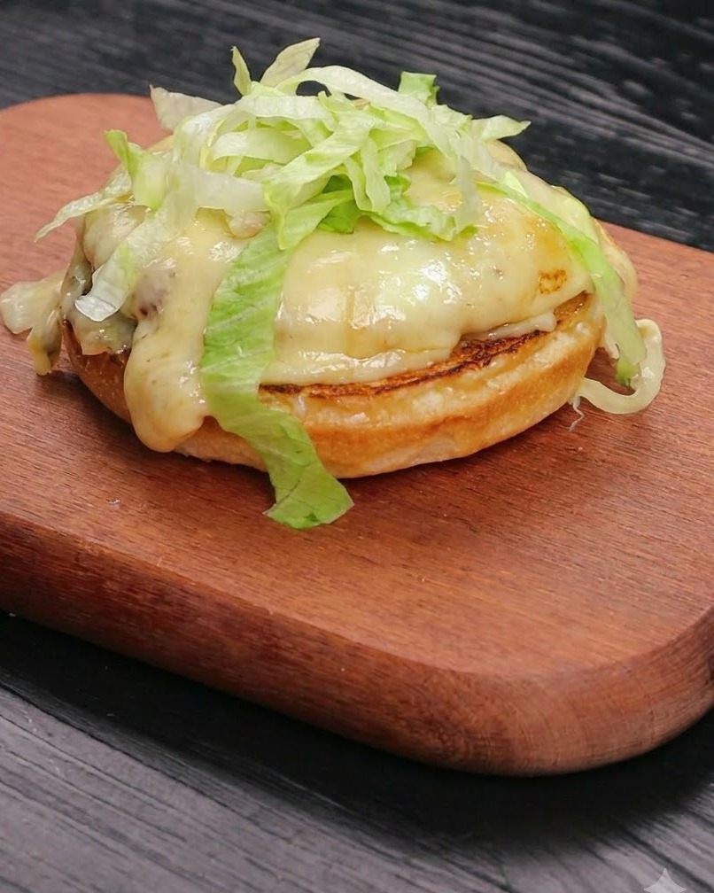 Frischer, geschnittener Salat liegt säuberlich auf einem geschmolzenen Käse- und Rinderpatty, das auf einer getoasteten Brötchenbasis ruht.