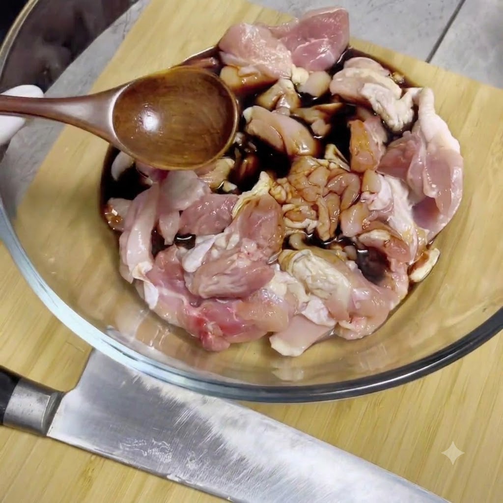 Sojasoße wird aus einem Holzlöffel auf rohe Hähnchenstücke in einer Glasschüssel gegossen.