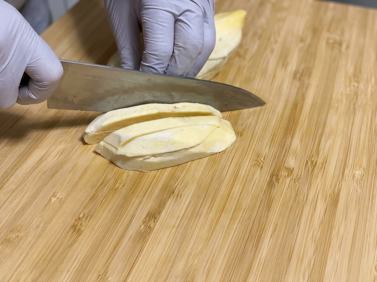 Geschälte rohe Süßkartoffeln werden mit einem Messer in lange Stifte auf einem Holzbrett geschnitten.