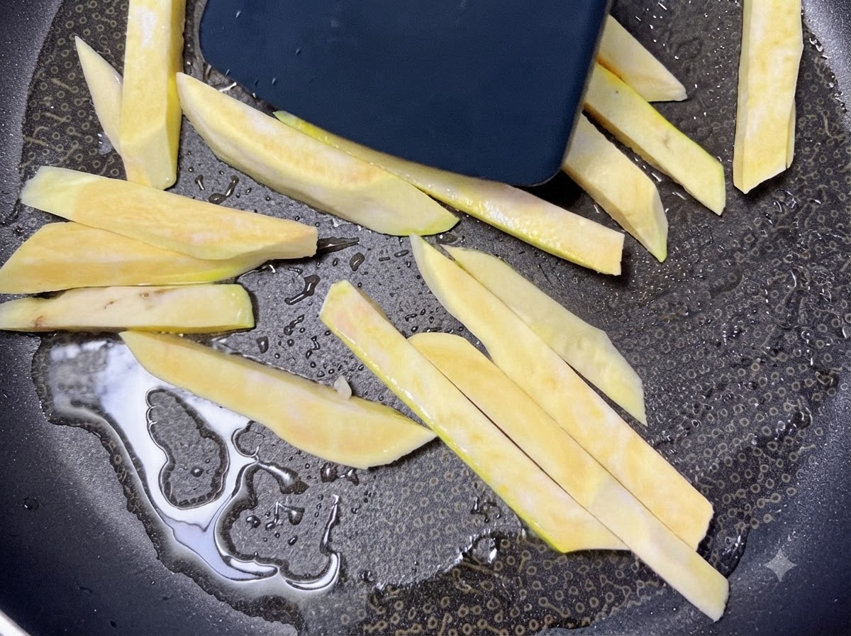 Rohe Süßkartoffelstifte brutzeln in einer heißen schwarzen Pfanne mit Öl und werden mit einem Spatel bewegt.